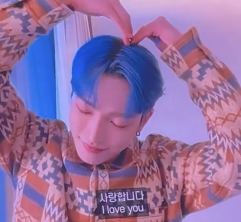 screenshot of hongjoong from ateez in blue hair, making a heart over his head